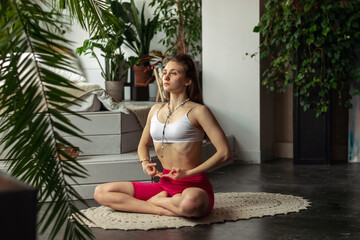 Young sporty woman practicing breathing yoga pranayama at home,sitting in Lotus position,holding...