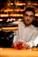 Focus on cup of shaker with strainer and glass and process of pouring cocktail