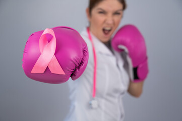 Female doctor in pink boxing gloves with a pink ribbon on a gray background. Fight against breast...