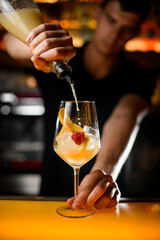 Close-up of beautiful glass with ice and lemon slices and raspberry in which bartender pours syrup from bottle