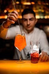 hand of male bartender stirs cocktail in glass on bar counter with spoon. Close-up.