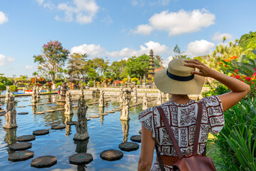 Woman traveler wearing white dress and straw hat at Taman Tirtagangga temple on Bali, Indonesia in a sunny day