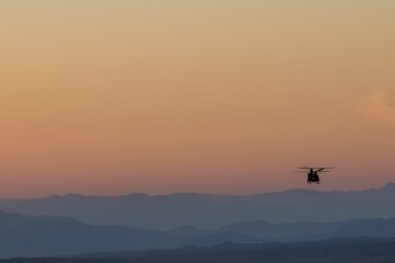 Silhouette of helicopter in orange sunset sky with silhouettes of mountains