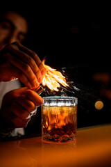amazing view on glass with drink on bar and male hand sprinkles by zest and sets it on fire