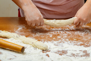 The hands of a Jewish woman make challah for a festive meal from dough.