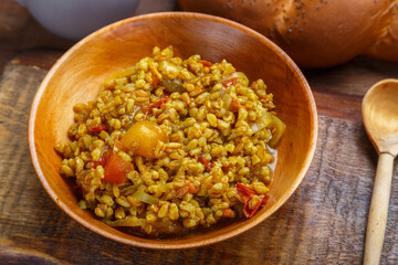 Spelled with vegetables and turmeric in a wooden plate next to a wooden spoon on a handmade wooden board.