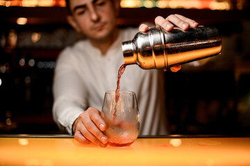 hand of male bartender carefully holds shaker and pours cocktail into glass