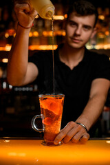 bartender masterfully adds syrup to tea with lemon slices in transparent cup on the bar