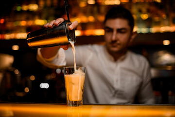 selective focus on shaker with strainer from which pours cocktail into glass with ice