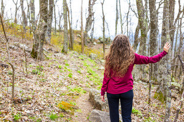 One lonely woman standing leaning against bare tree trunk in forest on Devil's knob hiking woods trail in Wintergreen ski resort, Virginia
