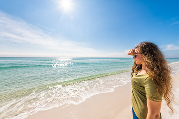Shiny glitter shimmer waves with young woman in sunglasses protecting eyesight with hand on forehead head from sun at Miramar, Florida Gulf of Mexico