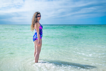 Fototapeta na wymiar Young female woman in one piece swimsuit standing inside ocean turquoise water paradise in Seaside, Florida Gulf of Mexico beach on panhandle