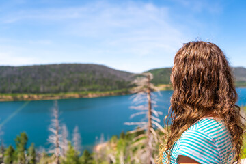 Young woman back looking at view of Navajo lake Kane county water reservoire in Utah with pine...