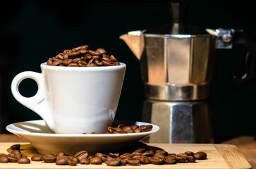 Closeup shot of a bunch of coffee beans in a cup and a coffee brewing machine near