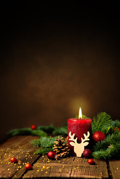 Kerze zum 1. Advent und Weihnachten. Dekoration mit roter Adventskerze, Tannenzweigen, Zapfen, Kugeln und Rentier auf Holz. Hochformat mit Textraum