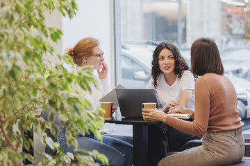 Fototapeta premium three female friends or colleagues are working and doing brainstorming. students or business partners in coworking create a project. young successful women entrepreneurs and designers. small business
