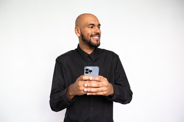 Portrait of happy young man holding mobile phone and looking away. Bearded businessman wearing black shirt smiling against white background. Mobile technology concept