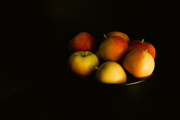 Red and yellow apples in a dark bowl on dark background in chiaroscuro style