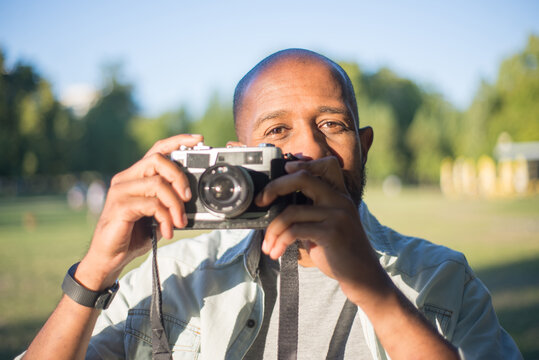 Close-up of happy African American man holding photo camera. Handsome bearded man standing in park looking at camera getting ready to take picture by himself. Leisure,hobby,modern technologies concept