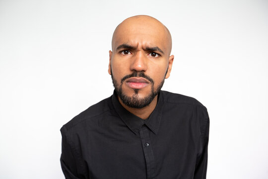 Portrait of frowning young businessman staring at camera against white background. Close-up of surprised face of bearded man wearing black shirt. Amazement concept