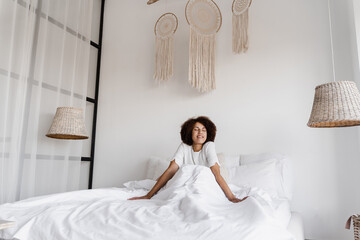Awakening african girl in bed at home and enjoying morning. African american girl woke up and sit...