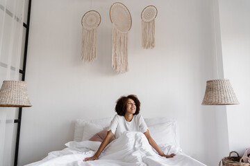 Awakening african girl in bed at home and enjoying morning. African american girl woke up and sit...