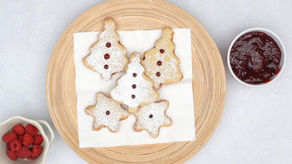 Homemade Christmas cookies with raspberry jam and powdered sugar topping close up on wooden plate directly from above