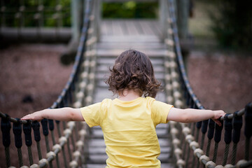 little boy plays in a playground on his own challenge crossing bridge