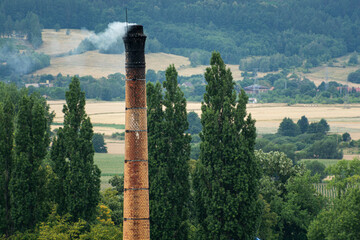 dymiący komin wykonany z cegły, w tle góry, lasy i pola
