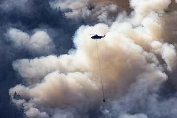 Wildfire Service Helicopter flying over BC Forest Fire and Smoke on the mountain near Hope during a hot sunny summer day. British Columbia, Canada. Natural Disaster