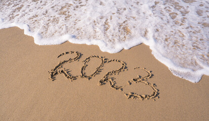 Hand-drawn numbers 2023 of new year on wet yellow sand on beach, copy space