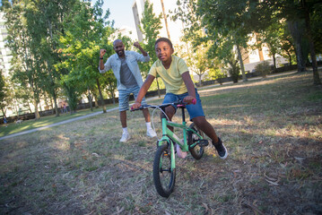 Portrait of happy dad and son having fun with bike. Smiling bearded man and little boy having active rest training to ride bike in summer park. Parenting, leisure, healthy growing-up concept