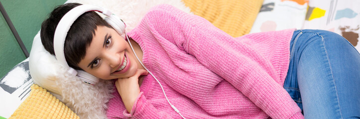 Obraz na płótnie Canvas Young smiling woman lying in bed using laptop and headphones