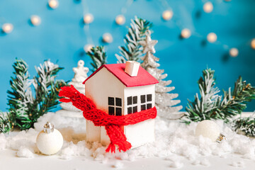 Abstract Advent Christmas Background. Toy house with knitted scarf with snow and winter decorations ornaments on blue background. Christmas with family at home concept.