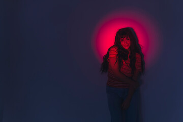 Modern aesthetic viral lamp photoshoot. Red light projector illuminating face and arms of beautiful young adult girl in striped t-shirt. Long, black, wavy hair with bangs. Studio shot. High quality