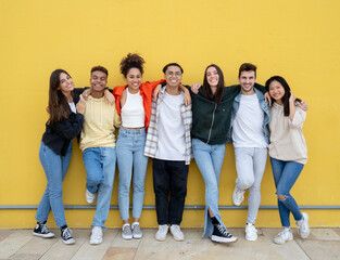 Group of young multiethnic friends laughing looking at camera on a yellow wall. Friendship and diversity concept