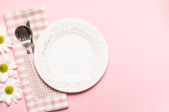 Country style tabble setting with plate, checkered napking, cutlery set and fresh chamomile flowers on light rose background with copy space for your design.