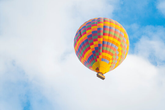 Patterned colourful hot-air balloon flying on the cloudy blue sky background above Turkish town of Cappadocia. Extreme sports and experiences during traveling. High quality photo