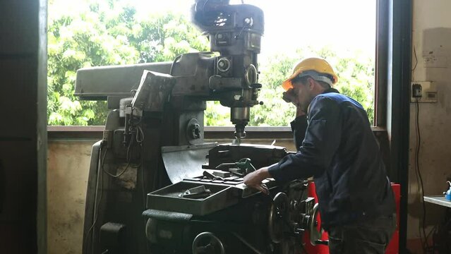 Technician wearing safety helmets and safety glasses works in a lathe shop : Male worker technician working on steel drill bit in industrial shop.