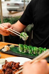 Vertical shot of chopsticks holding a sushi roll decorated with fresh seaweed served at a restaurant