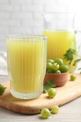 Tasty gooseberry juice and fresh berries on light wooden table, closeup