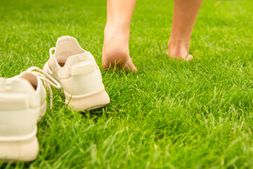 Woman leaving her sneakers and walking away barefoot on green grass, closeup
