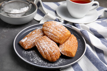 Delicious madeleine cakes with powdered sugar on grey table