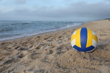Obraz premium Colorful volleyball ball on sand near sea. Space for text