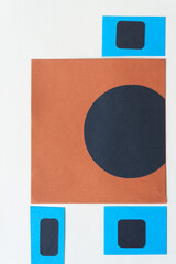 black circle on brown paper and black squares on blue paper