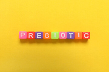 Colorful cubes with word Prebiotic on yellow background, flat lay