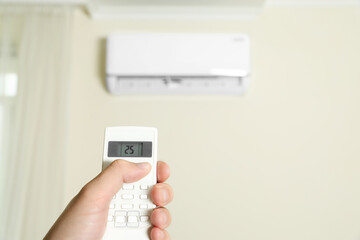 Man operating air conditioner with remote control indoors, closeup