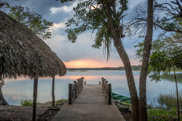 Wooden construction and wood deck next to fresh water lagoon in the tropical green jungle during golden hour at sunset with cloudy sky