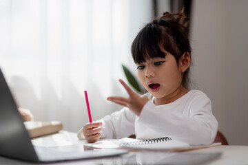 Little Asian girl doing her homework with laptop.