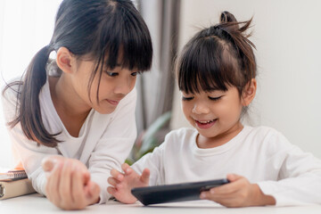 Asian kid girl having fun at home, using smartphone and laughing, playing video games on a mobile phone. kids and gadgets concept
